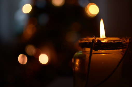Close up of a candle burning with flame in the dark. Warm candlelight on the black background with bokeh