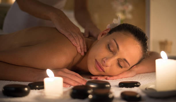 Candle light scene of woman in spa center Young woman laying on front receiving shoulder massage by professional therapist. Entire scene is shot with candle light only. basalt column stock pictures, royalty-free photos & images