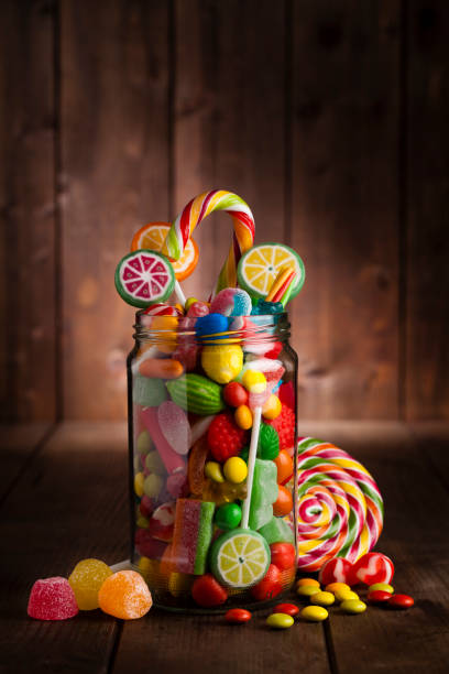 Candy jar on rustic wooden table Front view of an open candy jar filled with multi colored candies and jelly beans standing on rustic wooden table. Some candies are spilled out of the jar directly on the background. DSRL low key studio photo taken with Canon EOS 5D Mk II and Canon EF 100mm f/2.8L Macro IS USM candy jar stock pictures, royalty-free photos & images