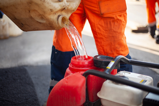 Canister of gasoline. Diesel engine refueling. Worker pours fuel into tank. Guy in orange clothes holds container of fuel.