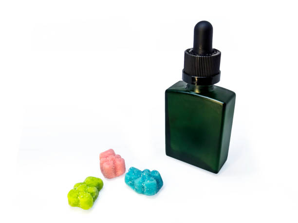 Cannabis extract oil in a green tincture bottle next to some CBD gummies Cannabis extract oil, known as CBD, in a green tincture bottle next to some CBD gummies on a white background organic cbd gummies stock pictures, royalty-free photos & images