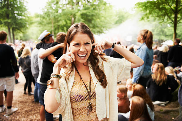 I can't hear you! A young woman struggling to hear on her smartphone at an outdoors festival Fingers in Ears stock pictures, royalty-free photos & images