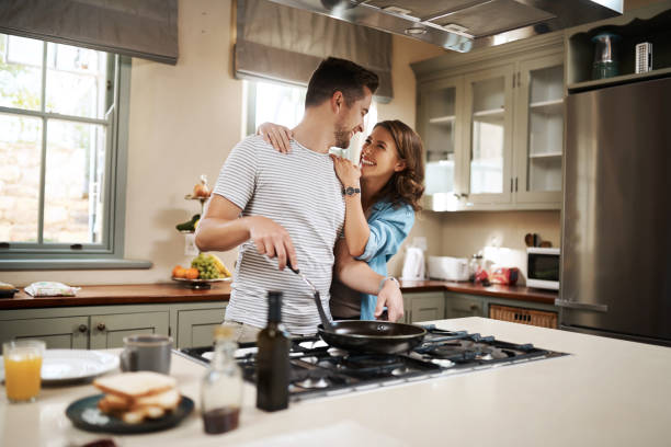 I can't wait to taste those eggs Shot of a young woman embracing her partner while he cooks breakfast stove stock pictures, royalty-free photos & images