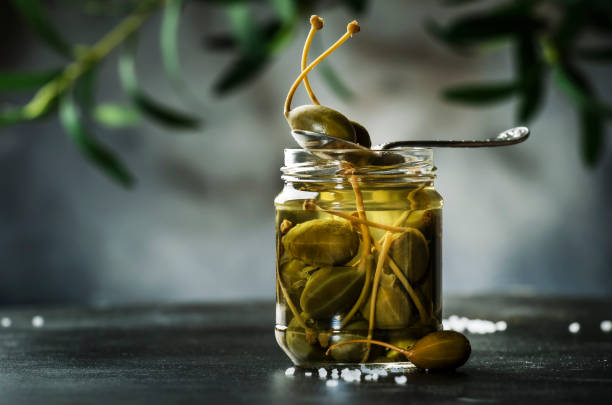Capers. Marinated or pickled canned capers fruit close up in glass jar on gray kitchen table background. Copy space Capers. Marinated or pickled canned capers fruit close up in glass jar on gray kitchen table background. Copy space caper stock pictures, royalty-free photos & images