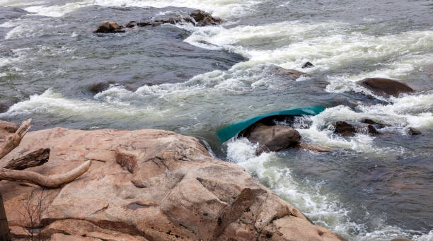 Capsized Canoe Capsized green canoe wedged between rocks and whitewater rapids in the James River Richmond, Virginia. capsizing stock pictures, royalty-free photos & images