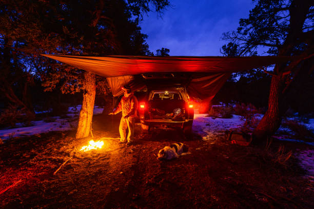 Car Camping Bushcraft with Tarp in Winter Car Camping Bushcraft with Tarp in Winter - Campfire and man enjoying the outdoors with tarp stretched over truck as shelter. Hanging out in back of truck relaxing and staying warm in winter outdoor adventure. bushcraft stock pictures, royalty-free photos & images
