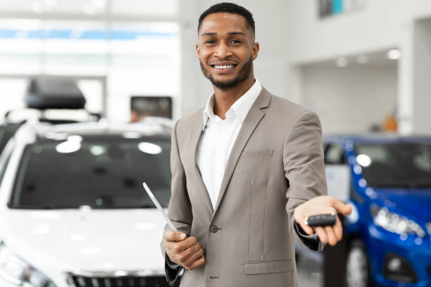 Car Dealer Offering Automobile Key To Camera Standing In Dealership Car Dealer Guy Offering Automobile Key To Camera Smililng Standing In Auto Dealership Store. Selective Focus car salesperson stock pictures, royalty-free photos & images