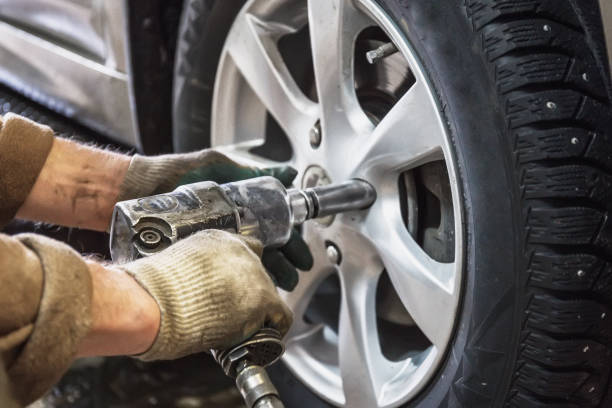 Car mechanic replace car wheels of lifted automobile by pneumatic wrench at repair service shop garage station stock photo
