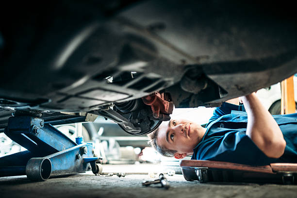 Car Mechanic Working Under Vehicle Low angle view of a mechanic working under a vehicle. brake stock pictures, royalty-free photos & images