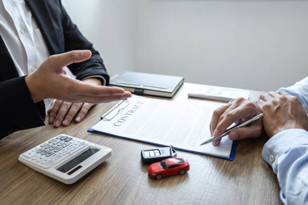 Car rental and Insurance concept, Young salesman presenting promotion and receive money and giving car's key to customer after sign agreement contract with approved good deal for rent or purchase stock photo