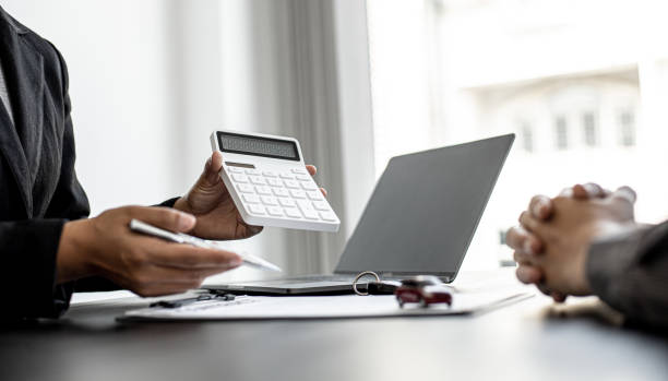 A car rental company employee holds a white calculator to show the tenant the rental price, the employee calculates the cost of the car rental before entering into the lease agreement with the renter. stock photo