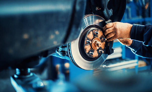 Car service procedure. Closeup of unrecognizable mechanic replacing car brake pads. The car is lifted with hydraulic jack at eye level. auto repair shop photos stock pictures, royalty-free photos & images
