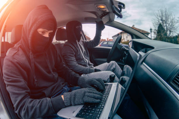 Car thief disarming car protections with laptop computer Car thief disarming car protections with laptop computer ski mask criminal stock pictures, royalty-free photos & images