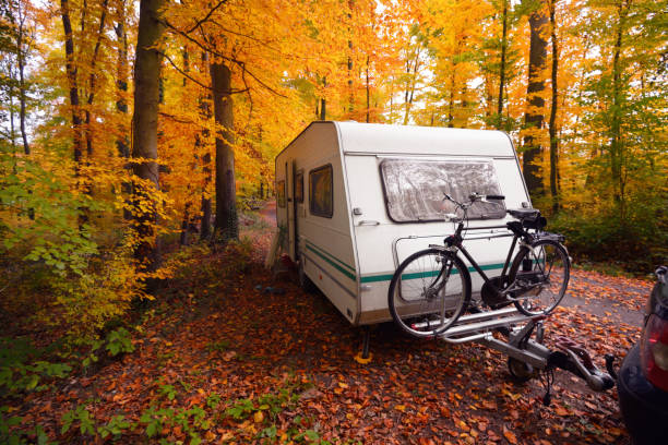 Caravan trailer with a bicycle and a car parked in a golden beech tree forest. Colorful red, orange and yellow leaves on the ground. Autumn landscape. Leisure activity in Heidelberg, Germany stock photo