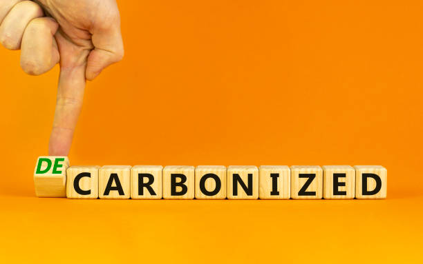 炭化または脱炭素化シンボル。ビジネスマンは木製の立方体を回し、「炭化」という言葉を「脱炭素化」に変えます。オレンジ色の背景、コピースペース。ビジネス、炭素化または脱炭素化� - 脱炭素 ストックフォトと画像