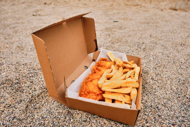 Cardboard box filled  with traditional Fish and Chips on the sand at Newquay, Cornwall on a June day. stock photo