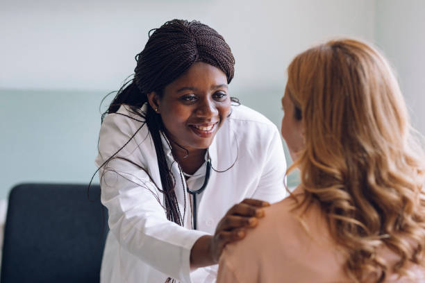 Care and Compassion and Trust: Smiling Doctor Lays her Hand on the Patient's Shoulder Smiling African American GP expressing care and support for her patient. patience stock pictures, royalty-free photos & images