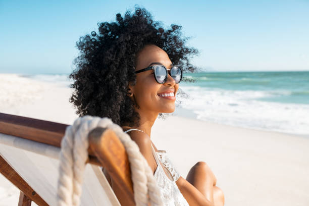 Carefree african woman relaxing on deck chair at tropical beach stock photo