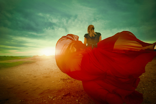 rear view of young woman with her red flying dress in the wind enjoying the sunset, the freedom and the silence of the moment. photo taken in wilderness area.