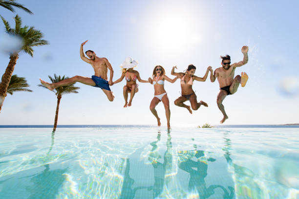 Carefree friends having fun while jumping into the pool. stock photo