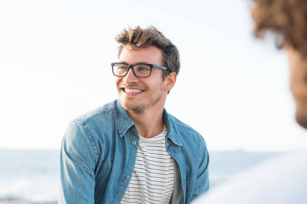 Carefree man Handsome man smiling at the beach and looking away. Portrait of a cheerful guy enjoying summer vacation. Handsome man with eyeglasses in casual relaxing outdoor with friend. young men stock pictures, royalty-free photos & images