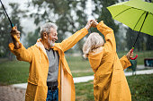 istock Carefree senior couple in raincoats dancing on a rainy day. 1367297292