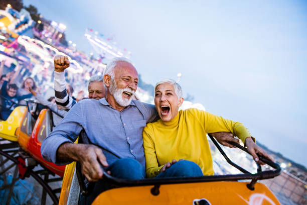 Carefree seniors having fun on rollercoaster at amusement park. Cheerful senior couple having fun while riding on rollercoaster at amusement park. Copy space. riding stock pictures, royalty-free photos & images