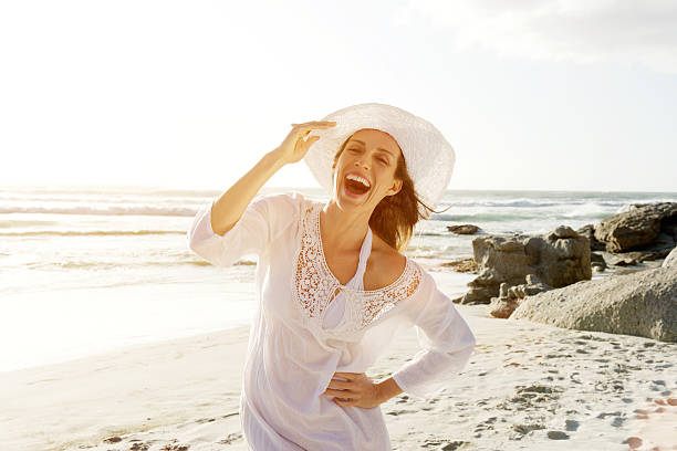 Carefree woman walking on beach with sun dress and hat Portrait of a beautiful carefree woman walking on beach with sun dress and hat mature women beauty beautiful fashion model stock pictures, royalty-free photos & images