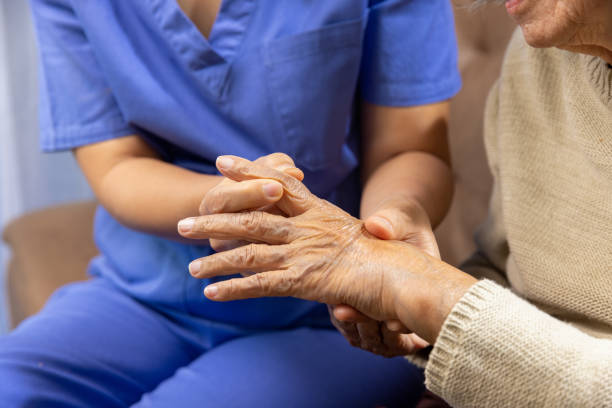 Caregiver massaging finger of elderly woman in painful swollen gout . stock photo
