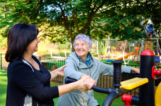 A caretaker holds the old woman as she gets into a fitness machine. stock photo