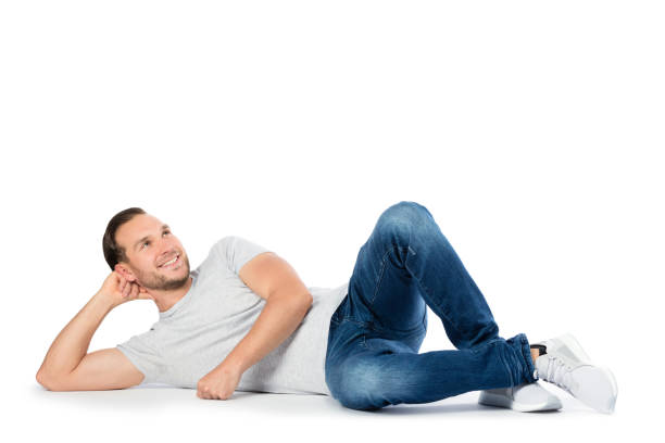 Carfree man laying on the floor, thinking. Cheerful man supporting his head on the hand, laying on the floor and looking up. Wandering happy thoughts. Isolated on white background. lying down stock pictures, royalty-free photos & images