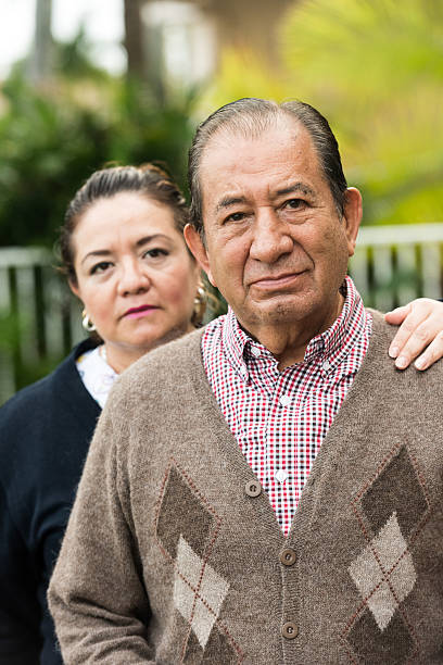 caring, hispanic nurse and elderly senior patient in nursing home - embrace man woman serious stockfoto's en -beelden