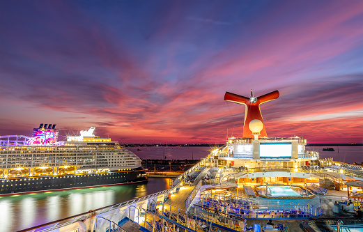 Port Canaveral, Florida, USA - September 5, 2019: Carnival Liberty and Disney Dream cruise ships docked in Port Canaveral at sunset. Beautiful red-orange-blue sunset sky in the background.
