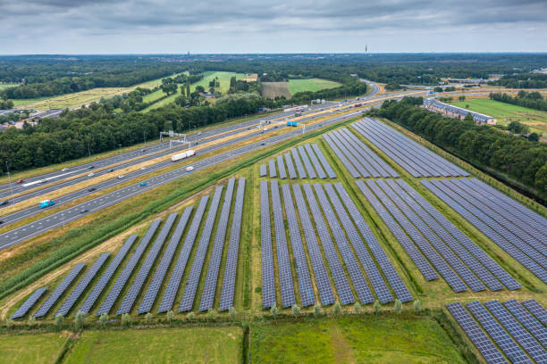 Cars driving on road passing by solar panels farm for producing green ecological electricity stock photo