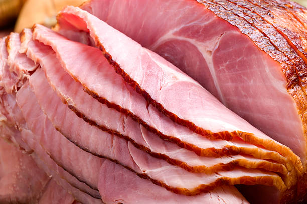 Carved slices of ham folding on top of one another Closeup of delicious whole baked sliced ham with fresh strawberries and figs on holiday table. ham stock pictures, royalty-free photos & images