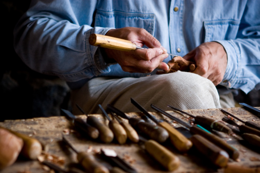 An experienced carpenter shapes wood with a chisel.