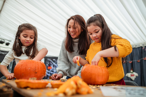 Mother and daughters carving pumpkins at a farm after picking them at a farm in preparation for Halloween.