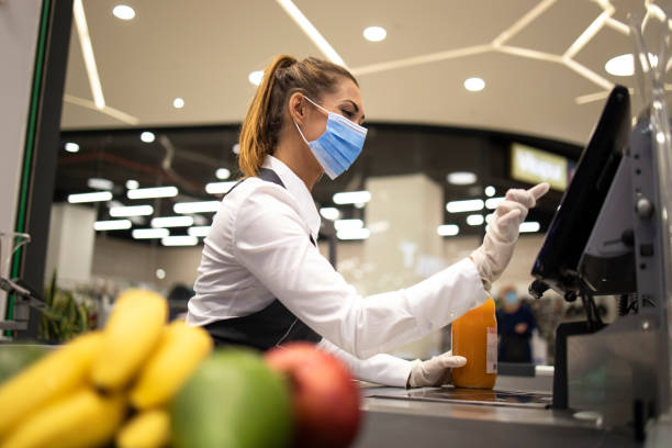 Cashier with protective hygienic mask and gloves working in supermarket and fighting against COVID-19 or corona virus pandemic. People endangered on their workplace because of corona virus. grocery store stock pictures, royalty-free photos & images