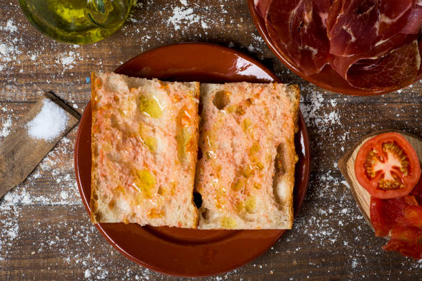 catalan pa amb tomaquet and serrano ham high-angle shot of typical catalan pa amb tomaquet, bread with tomato, placed on a plate, on a rustic wooden table next to a plate with some slices of serrano ham, tomato and a cruet with olive oil catalonia stock pictures, royalty-free photos & images
