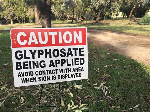 Perth, Wa - Mar 23 2021:Cation Glyphosate being applied. Outdoor sign on city park path. It is used to kill weeds, especially annual broadleaf weeds and grasses that compete with crops.