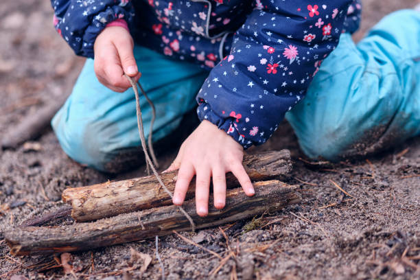 Caucasian child girl in warm winter clothing playing with twig and string stock photo