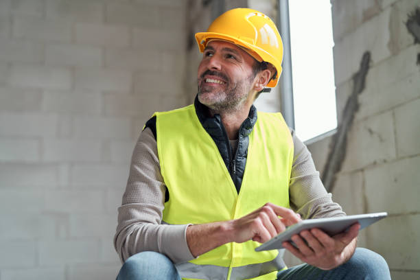 Caucasian engineer sitting on stairs and browsing digital tablet on construction site stock photo