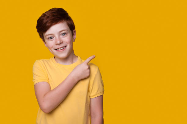 Caucasian ginger boy is advertising something pointing at the yellow studio free space stock photo