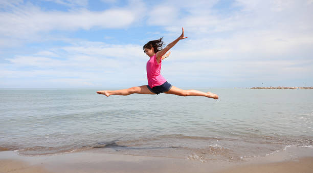Caucasian girl performing rhythmic gymnastics exercises and the split in the air with the sea in the background Caucasian girl performing difficult rhythmic gymnastics exercises and the split in the air on the beach with the sea in the background doing the splits stock pictures, royalty-free photos & images