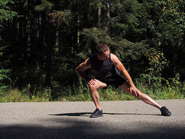 Caucasian male runner athlete stretching outdoors in forest stock photo