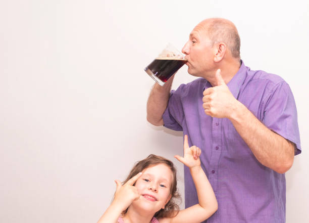 um homem caucasiano bebe uma bebida ou cerveja com prazer, e uma criança, uma menina, aponta o dedo para ele. - social media - fotografias e filmes do acervo