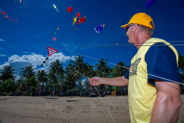 caucasian Man is flying a giant kite in a kite flying festive in a bright day with the blue sky in the background at a beach stock photo