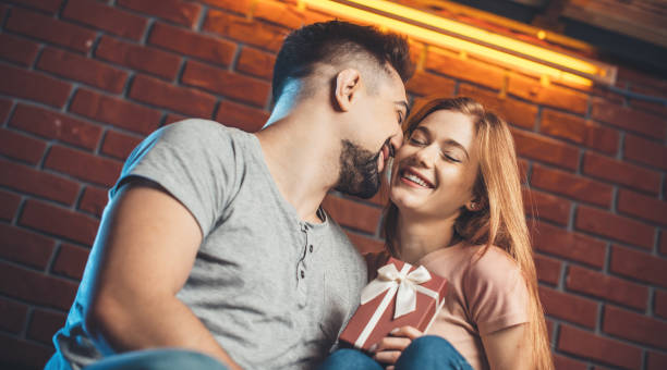 Caucasian man is kissing his girlfriend while giving her a present dating on valentines day stock photo