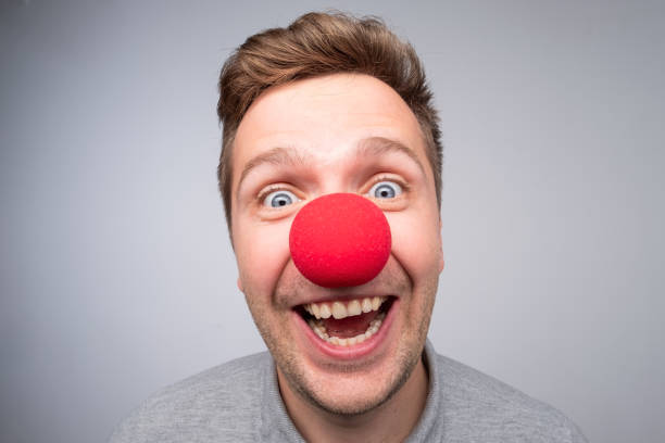 Caucasian man with crazy look wearing a clown nose Caucasian man with crazy look wearing a clown nose. Concept of happy birthday party, being in good mood clown's nose stock pictures, royalty-free photos & images