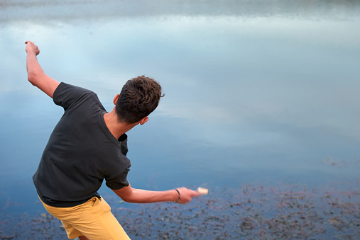 Caucasian man with yellow shorts is throwing stones into the lake